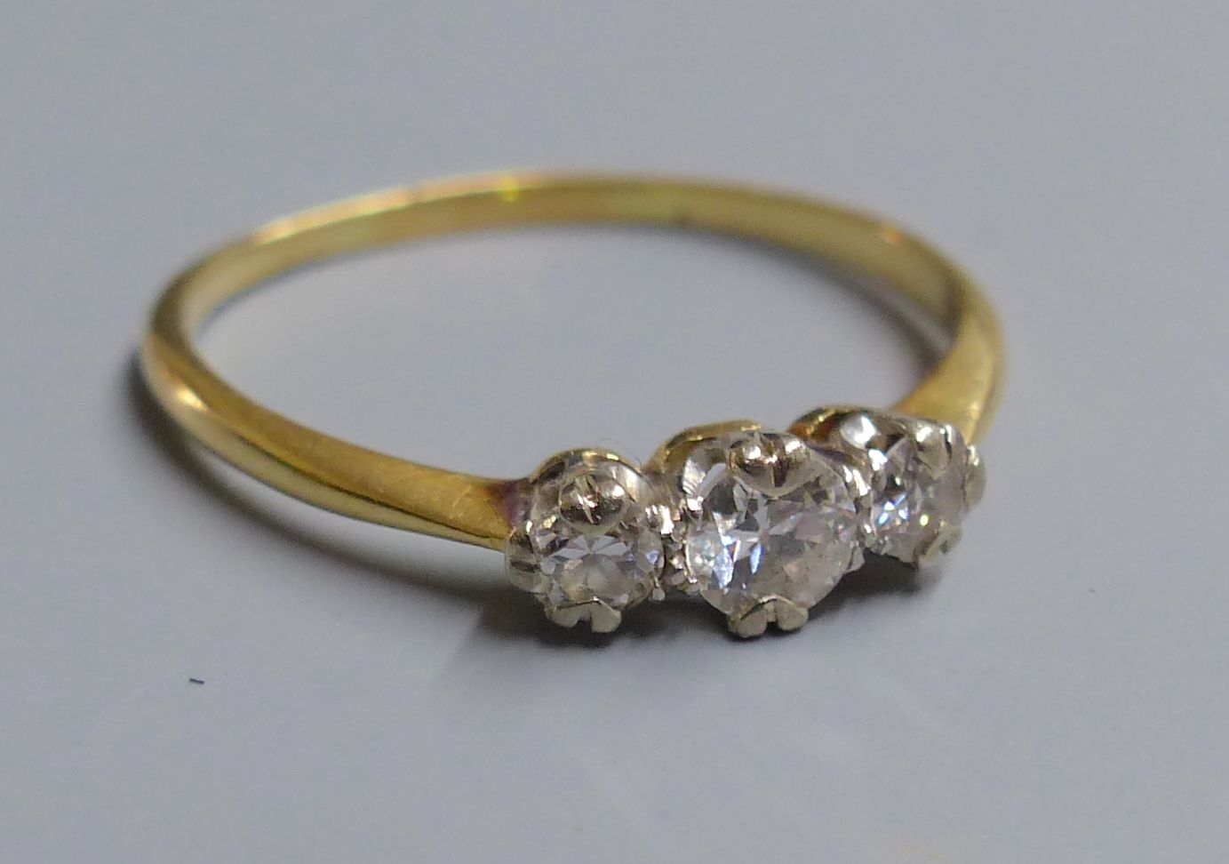 A yellow metal (tests as 18ct) and three stone diamond ring, size O, gross 2.2 grams.